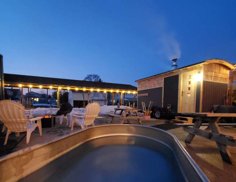 The sauna, cold plunge tub and fire pit lit at dusk